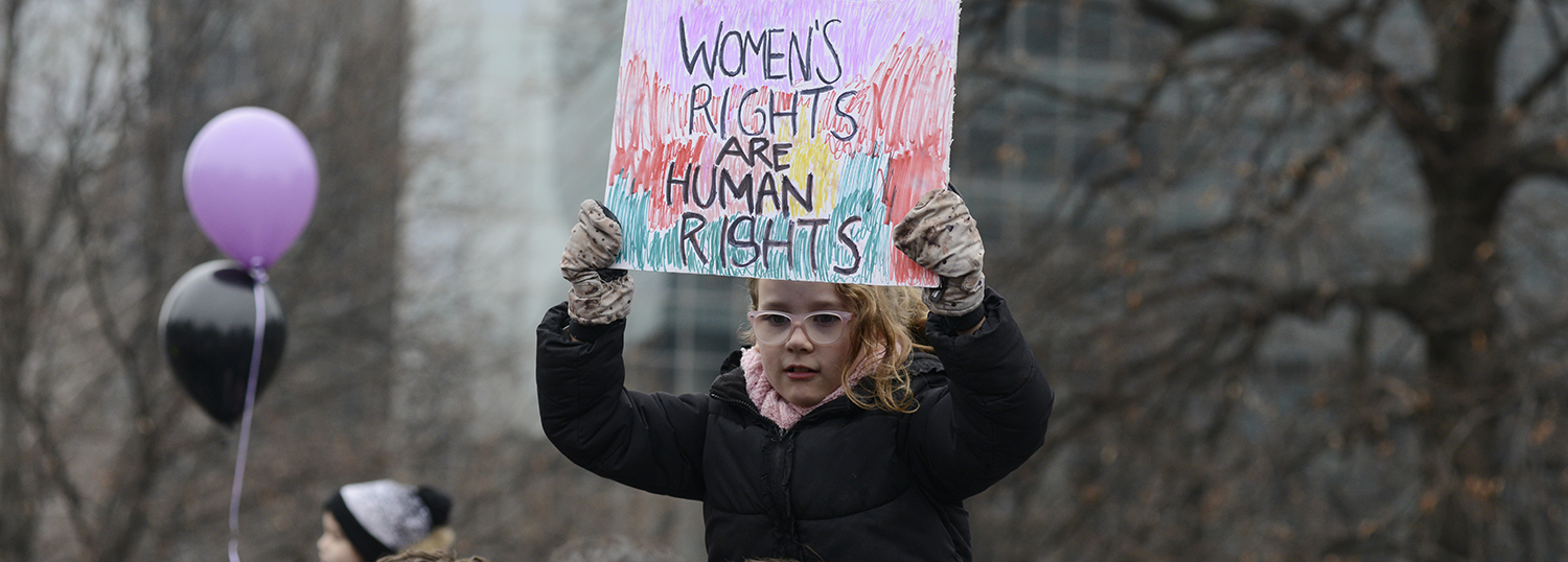 Een klein kind dat een spandoek draagt met de tekst 'vrouwenrechten zijn mensenrechten'