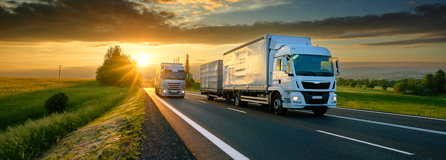 Vrachtwagens op een asfaltweg in een landelijk landschap bij zonsondergang
